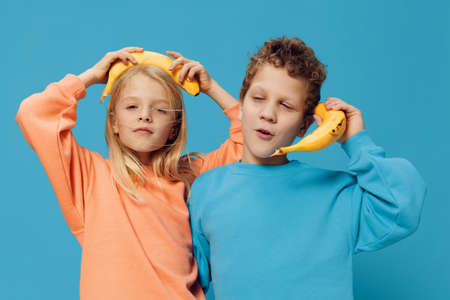 funny, cute children, a boy and a girl stand on a blue background in bright clothes and holding bananas in their hands pretend to be talking on the phoneの写真素材