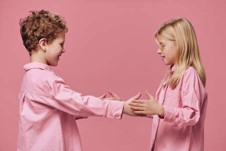 cute, beautiful, joyful children, a boy and a girl play with each other clapping their hands while standing in pink clothes on a pink background. Horizontal studio photographyの写真素材