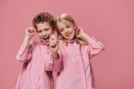 funny, happy children brother and sister play with each other standing on a pink background in pink clothes. Studio photo with an empty space for an advertising insertの写真素材