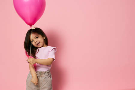 nice, little girl of preschool age plays with a pink balloon in her handsの写真素材