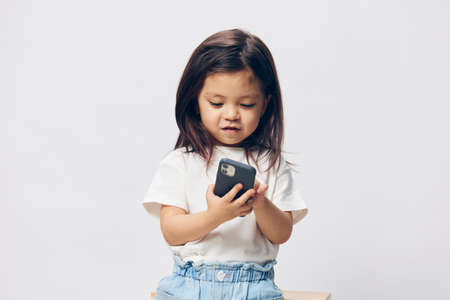 a cute little girl of preschool age is standing on a white background in a white T-shirt,...