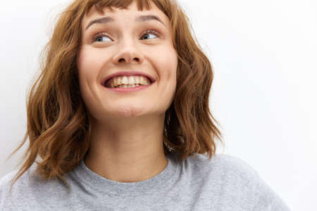 a happy, very joyful woman stands on a white background in a gray T-shirt smiling broadly expressing her emotions. Close horizontal photoの写真素材
