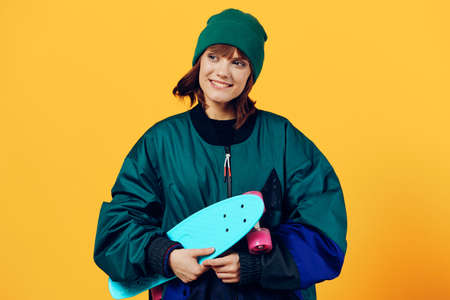 a joyful woman stands on a yellow background in a fashionable jacket and hat from the 90s and...