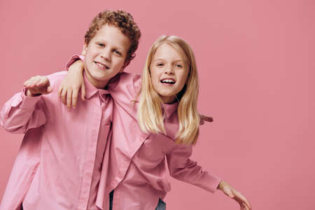 cute beautiful children stand in pink clothes on a pink background with their hands on each others...