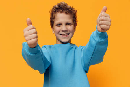 funny, emotional, cute boy stands on a yellow background with a very happy face and shows thumbs upの写真素材