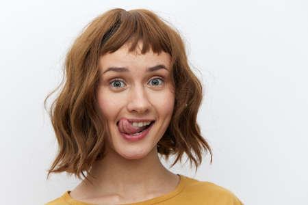 horizontal close-up portrait of a beautiful, playful woman in a yellow T-shirt on a light background amusingly showing her tongue to the cameraの写真素材