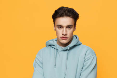 a handsome teenager stands on an orange background in a light hoodie and looks at the camera. Horizontal photoの写真素材
