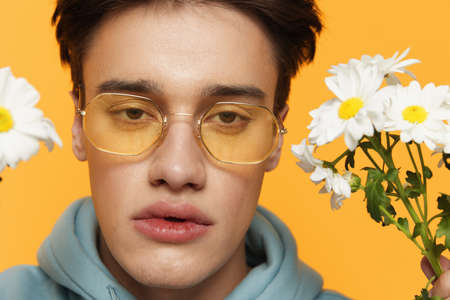 portrait of a handsome, attractive man in yellow sunglasses holding a bouquet of daisies near his...