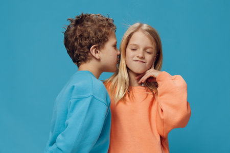 two cute children, school age in multi-colored sweaters stand on a blue background and the boy...