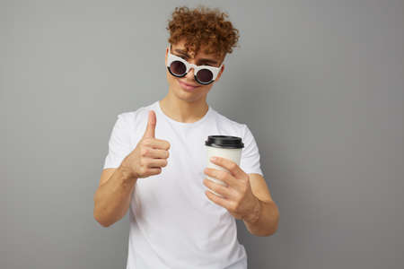 a young man of athletic build stands dressed in a white T-shirt, with sunglasses on his face and...