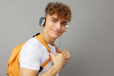 an attractive man with a backpack on his back is standing on a gray background listening to music in...