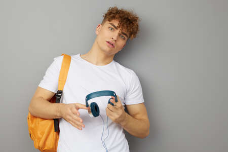 a relaxed student stands on a light gray background, looks at the camera with his back against the...