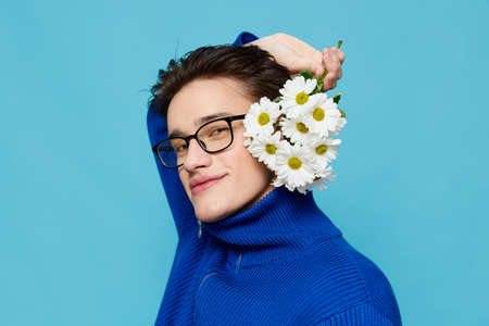 portrait of a handsome man in a blue zip-up sweater and black eyeglasses, standing modestly on a...