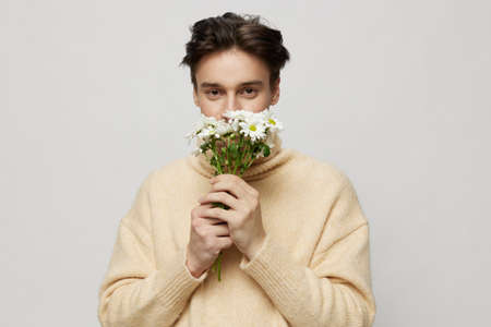 A handsome young man with fair skin with dark, short, beautiful hair combed back in a beige...