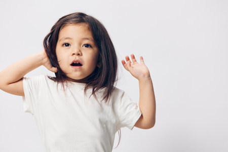 a little girl of preschool age, sitting on a white background in a white T-shirt, enthusiastically talking on the phone, turning half-side to the camera. The topic of the conversation on the phoneの写真素材