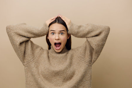 horizontal photo of an emotional, vividly expressing her emotions of a woman standing in a stylish sweater with her hands raised behind her headの写真素材