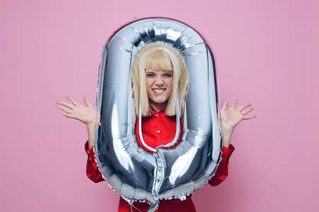 a funny, emotional woman stands on a pink background in a red shirt with an inflatable ball in the...