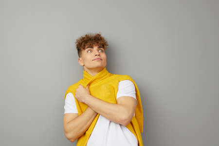 an attractive man stands on a gray background in a white T-shirt, wrapped in his yellow sweaterの写真素材