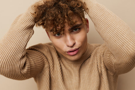 a charming, handsome man stands on a beige background in a sweatshirt and looking at the camera...