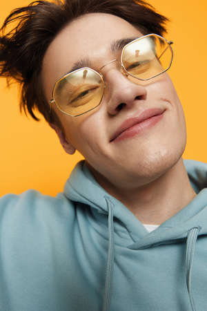 a close portrait of a funny man standing on an orange background in bright sunglasses looking at the camera with a smileの写真素材