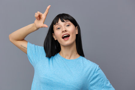 a surprised woman stands on a dark background in a blue T-shirt, raises her finger and opens her mouth wideの写真素材