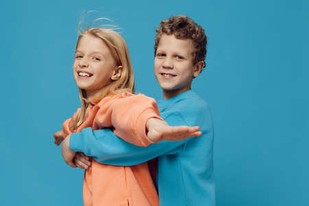 cute, beautiful, happy children, brother and sister stand in bright clothes on a blue background and the boy hugs the girl from the back. Studio photography with blank space for advertising mockupの写真素材