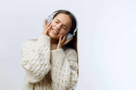 a close photo of a happy, cheerful woman standing holding headphones on her head, opening her mouth wide and closing her eyes with pleasureの写真素材
