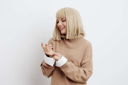 Horizontal photo, a woman on a white background in a beige sweater with beautiful blond hair looks joyfully to the side with her hands in front of herの写真素材
