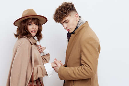 a happy couple in love is standing in beige stylish autumn coats on a white background and a man is holding a womans hand with his eyes closedの写真素材
