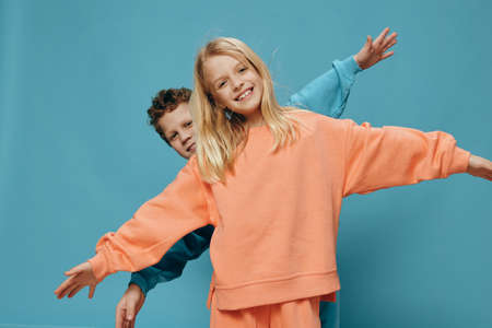 two cute children of school age in multi-colored sweaters stand on a blue background, a boy and a girl stand with their hands apart, depicting airplanes. The theme of friendship between childrenの写真素材