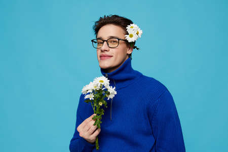 portrait of a handsome man in a blue zip-up sweater and black eyeglasses, standing modestly on a...