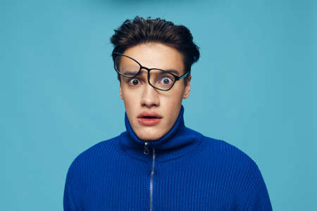 a handsome, attractive man stands on a light blue background in a blue zip-up sweater with...