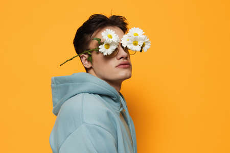 a close portrait of a handsome, funny man with daisies on his eyes, standing on a bright background...