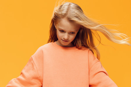 funny emotional girl stands on a bright background and looks down with her hair developing in the windの写真素材