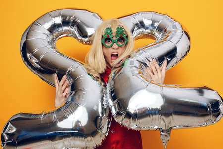 horizontal photo on a bright background of a happy, emotional woman in funny holiday glasses holding...