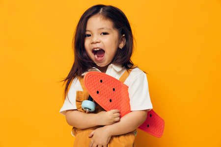 joyful, happy, little girl of preschool age in an orange sundress stands on an orange background...
