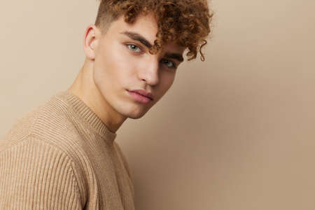 close horizontal portrait of a handsome, charming man with curly hair standing in a beige sweater on...