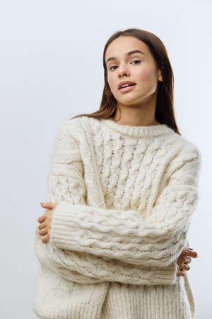 a beautiful, attractive, relaxed woman stands with her arms crossed on her chest in a white knitted...