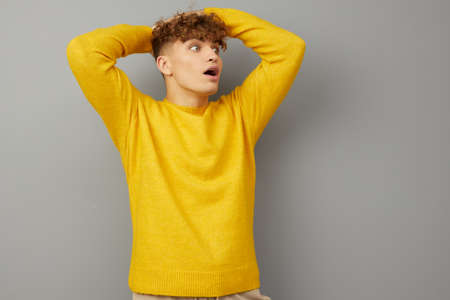 a surprised man stands on a gray background in a stylish yellow sweater and looks wide-mouthed to...