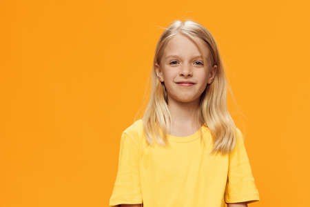 a cute, happy girl in yellow clothes stands on a yellow background and smiles sweetly at the camera. Horizontal studio photography on a plain background with empty spaceの写真素材