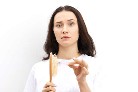 upset, pleasant woman with long black hair standing in a white T-shirt on a background and looking...
