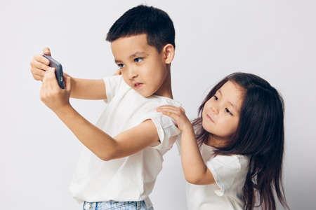 brother and sister take a selfie on their fashionable smartphone while standing in white T-shirts on a light background sideways to the cameraの写真素材