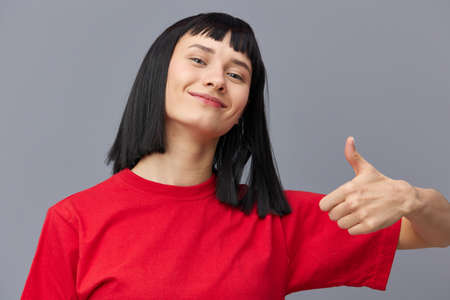 a close horizontal photo of a happy, joyful woman standing on a gray background and showing a big scumbag up in a sign of approval, joyfully looking into the cameraの写真素材