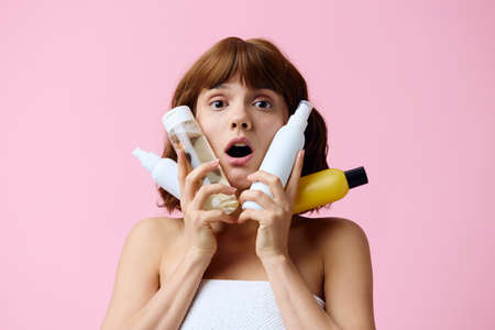 a happy woman stands on a pink background smiling happily and holding a white jar of cream in her hand looking at camera with smileの写真素材