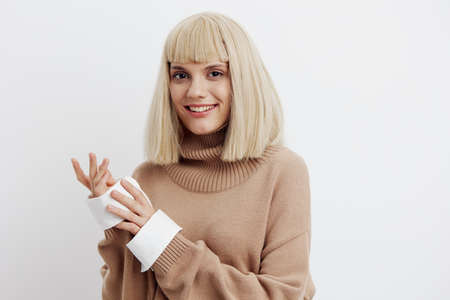 a woman on a white background in a beige sweater with beautiful blond hair joyfully looks at the...