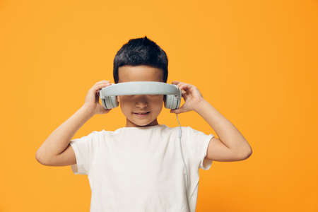 a cute, funny little boy stands on an orange background and listens to music in bright headphones...