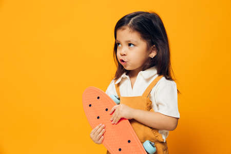 cute, funny, pensive little girl stands holding a skateboard in her hand looking away. Horizontal photo with empty space to insert an advertising layoutの写真素材