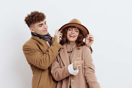 a sweet, loving couple stands on a white background in autumn clothes and the guy adjusts the hat on the head of a joyful woman looking at her with snow. Horizontal photoの写真素材