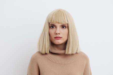 Horizontal photo, a woman on a white background in a beige sweater with beautiful blond hair seriously looks aheadの写真素材