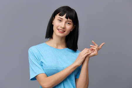 a calm woman stands against a dark background in a blue T-shirt smiling sweetly with her hands...